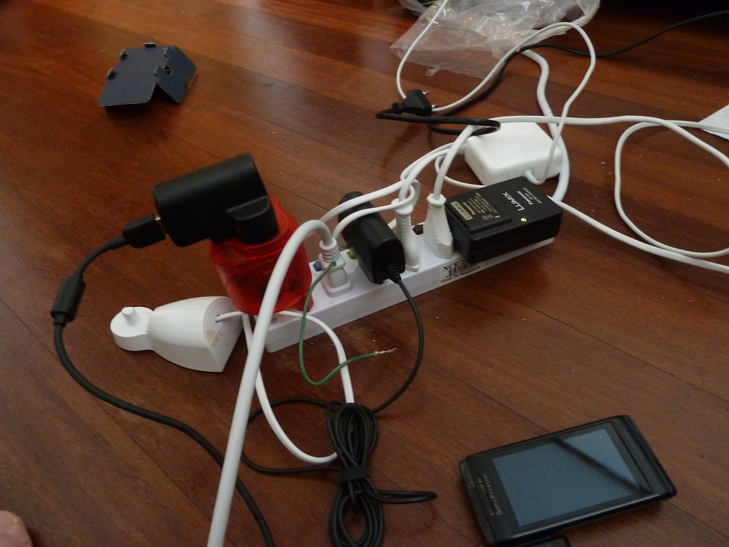 Régua de energia com vários cabos e adaptadores sobre uma superfície.